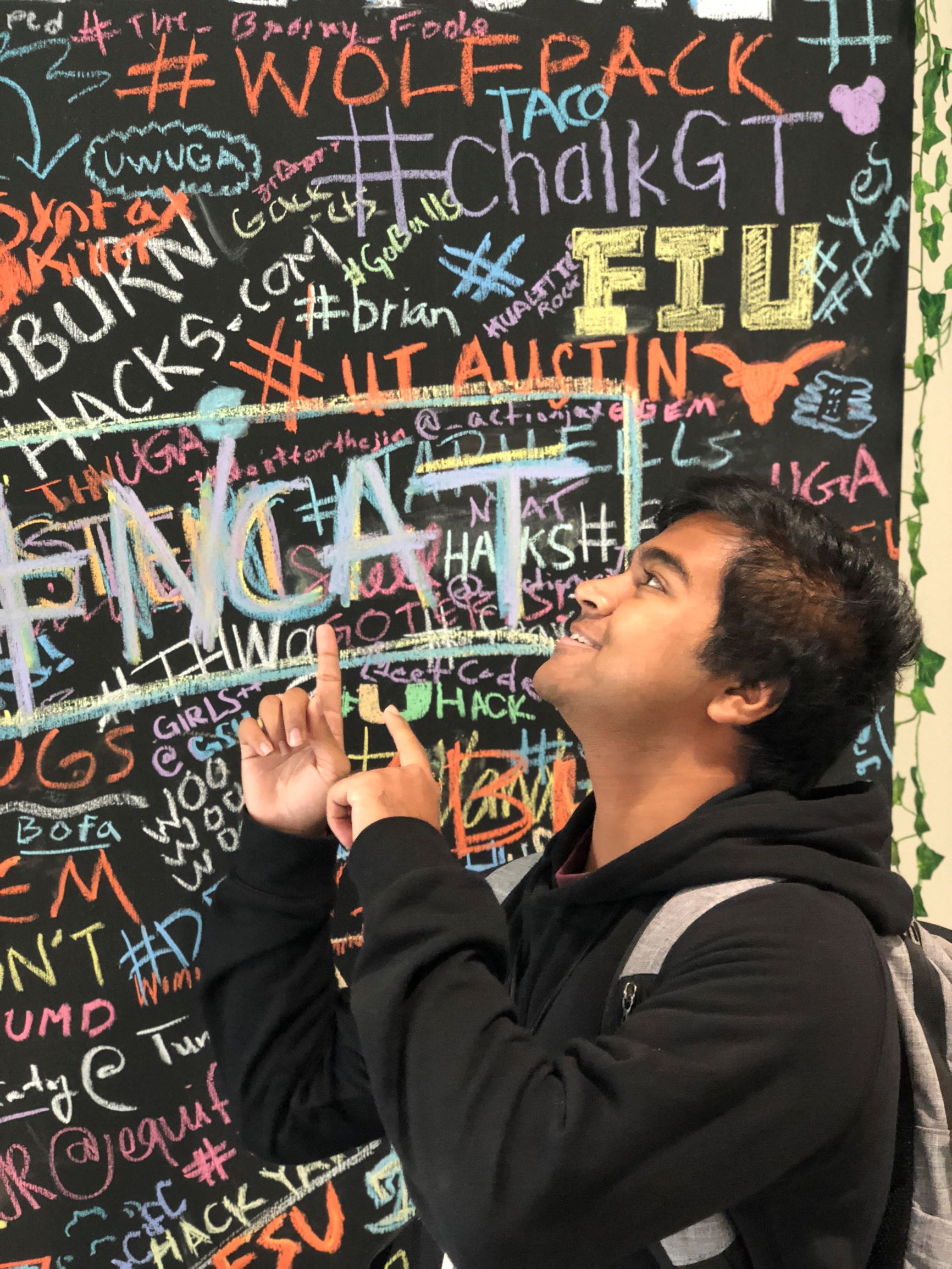 Picture of me looking up in front of the wall with college names at HackGT